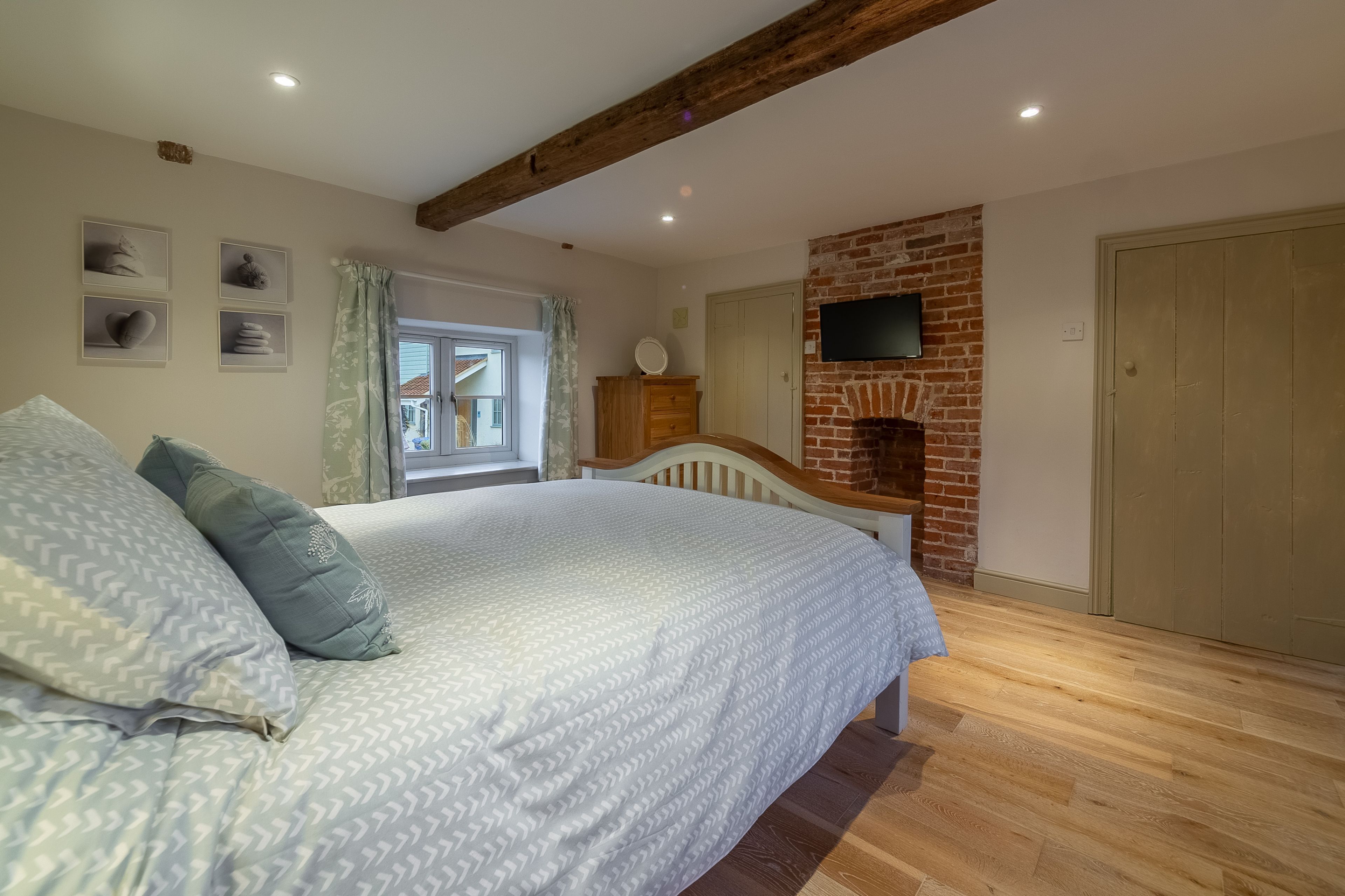 A bedroom with a large bed, wooden beams, a brick wall, a TV, and a window with curtains.