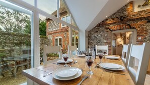A dining table set with plates, glasses, and cutlery in a room with brick walls and large windows. - Mayes Cottage, Brancaster, Norfolk (Brancaster)
