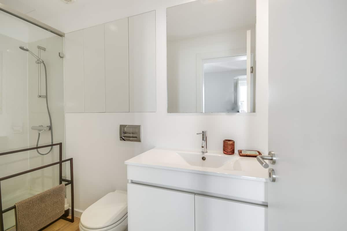 Un baño moderno con cabina de ducha de vidrio, un lavamanos blanco y un jabonera de color cobre, y un inodoro.