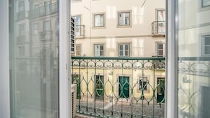 Una vista da una finestra con ringhiera in metallo, un edificio con numerose finestre e balconi, e una strada acciottolata.