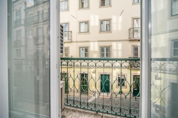A view from a window with a metal balcony railing, a building with multiple windows and balconies, and a cobblestone street. - Bairro House Lisbon Charming Suites (Lisbon)