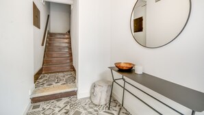 Una scala con piastrelle decorate, uno specchio tondo, uno sgabello di legno e un tavolino con una ciotola e una candela.