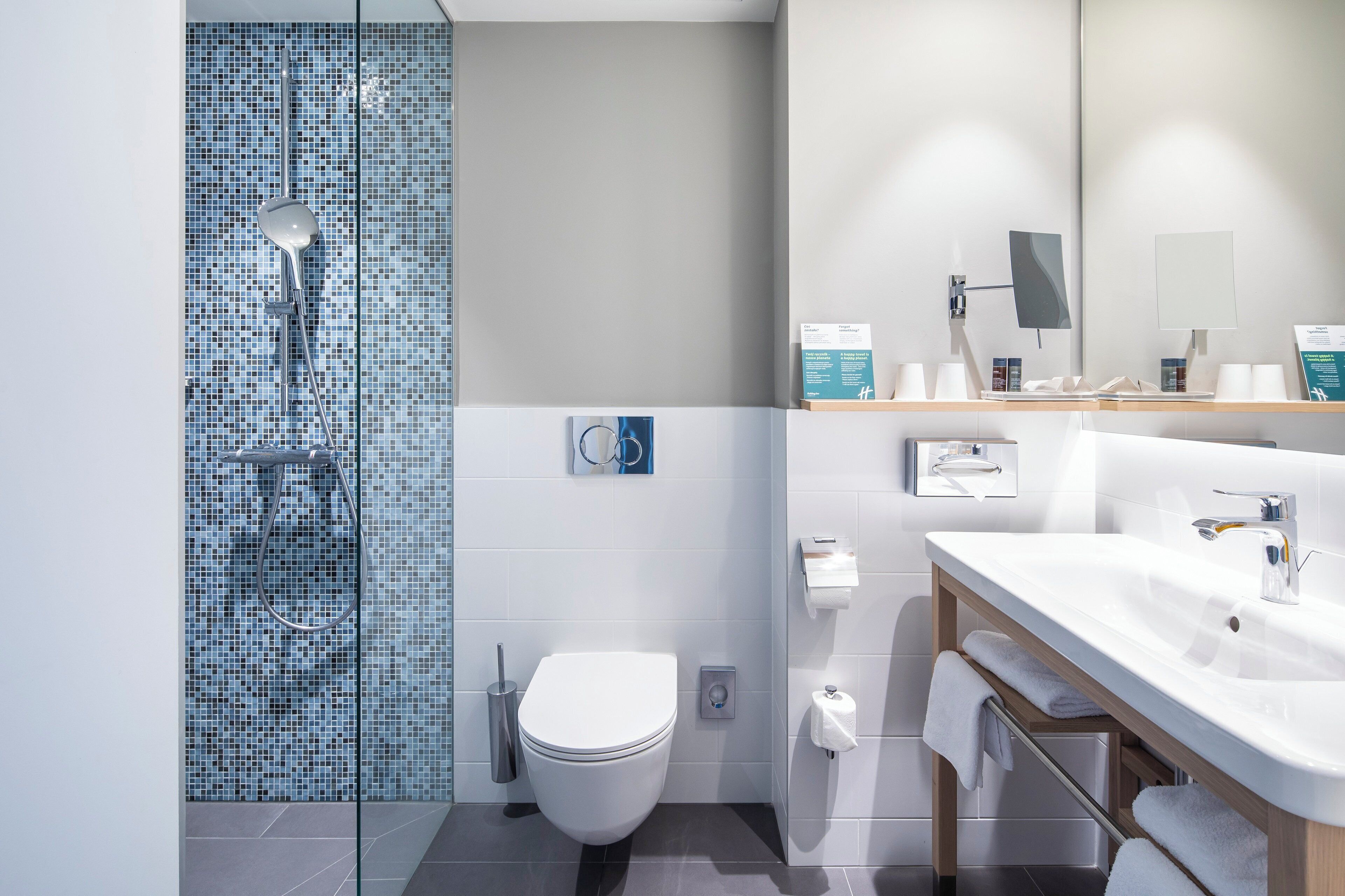 A modern bathroom with a glass shower enclosure, a white toilet, a sink with a mirror, and a towel rack.