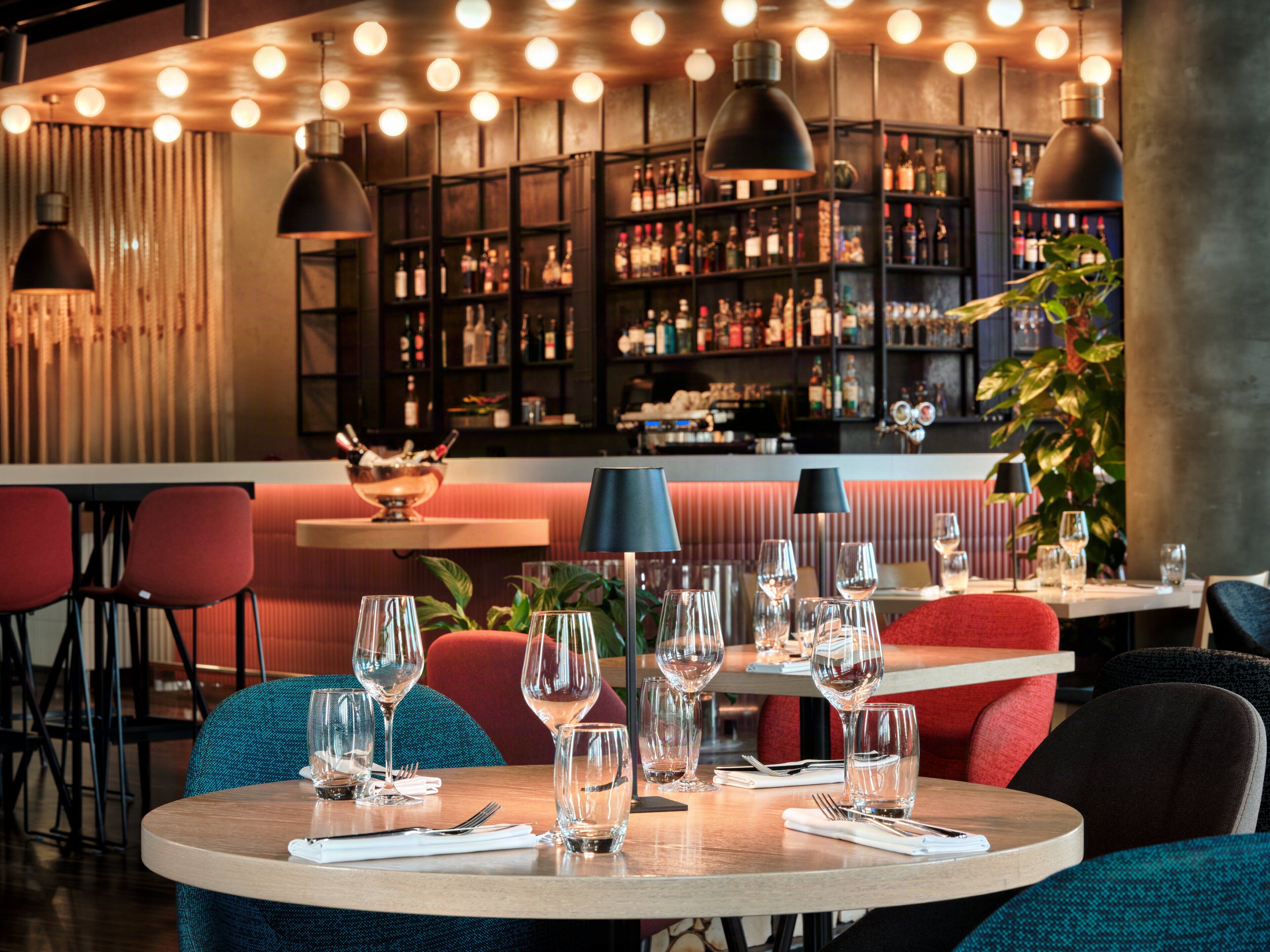A restaurant interior with round tables, chairs, and a bar area with shelves of bottles.