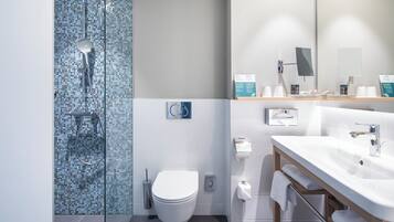 A modern bathroom with a glass shower enclosure, a white toilet, a sink with a mirror, and a towel rack.