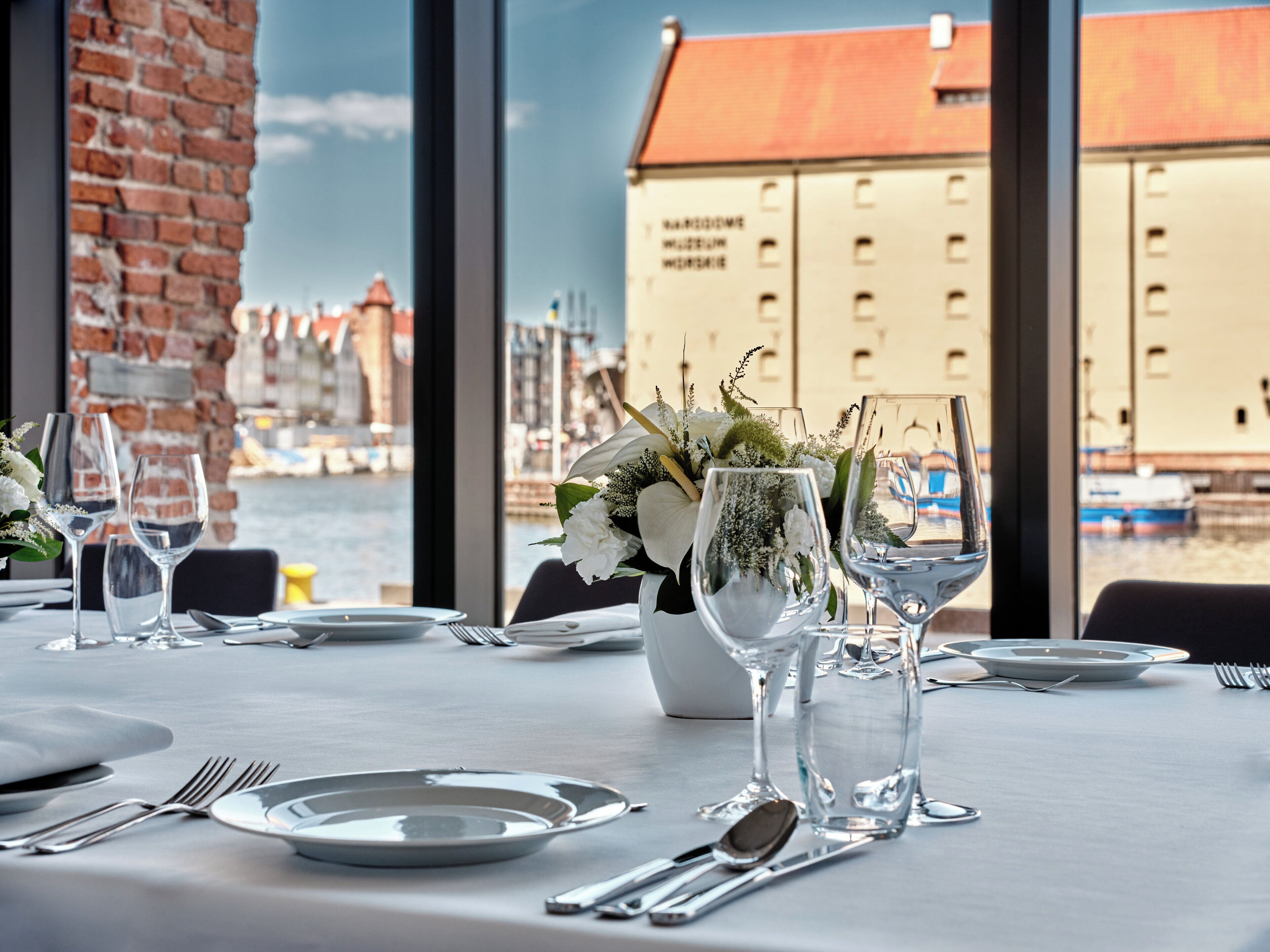 Una mesa preparada para comer con vista a un canal y edificios al fondo.