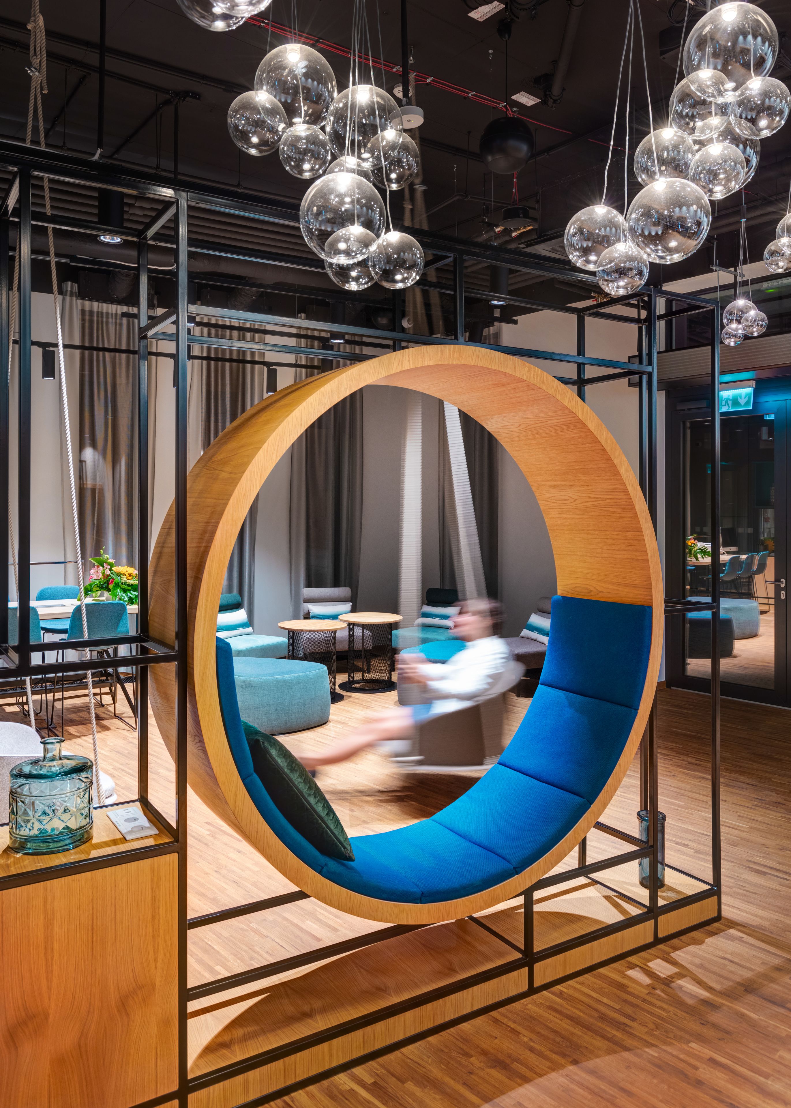 A modern interior with a circular wooden swing chair, wooden flooring, and hanging spherical light fixtures.