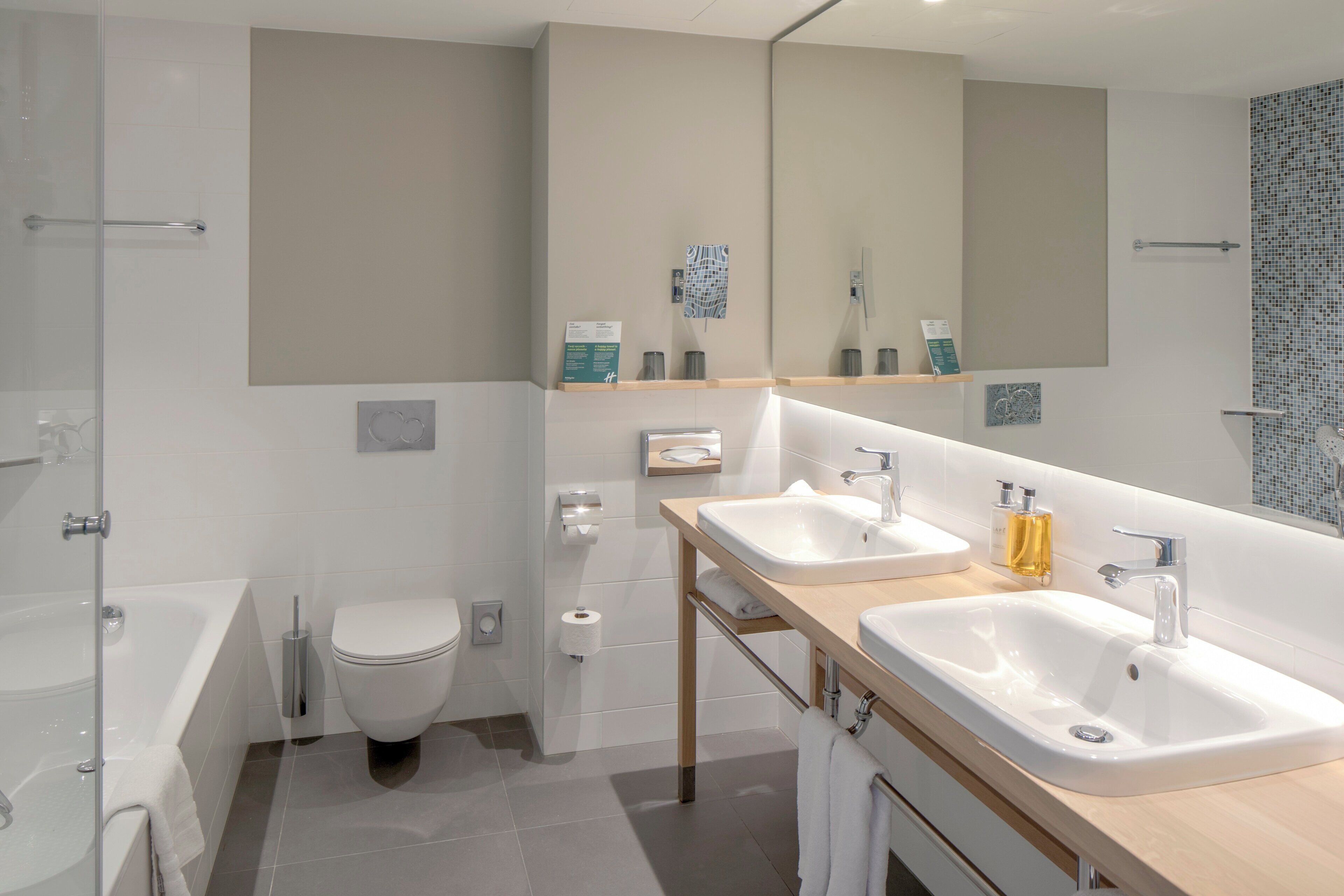 A modern bathroom with a bathtub, two sinks, a toilet, and a large mirror.