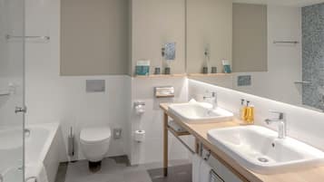 Un baño moderno con bañera, dos lavamanos, inodoro y un espejo grande.