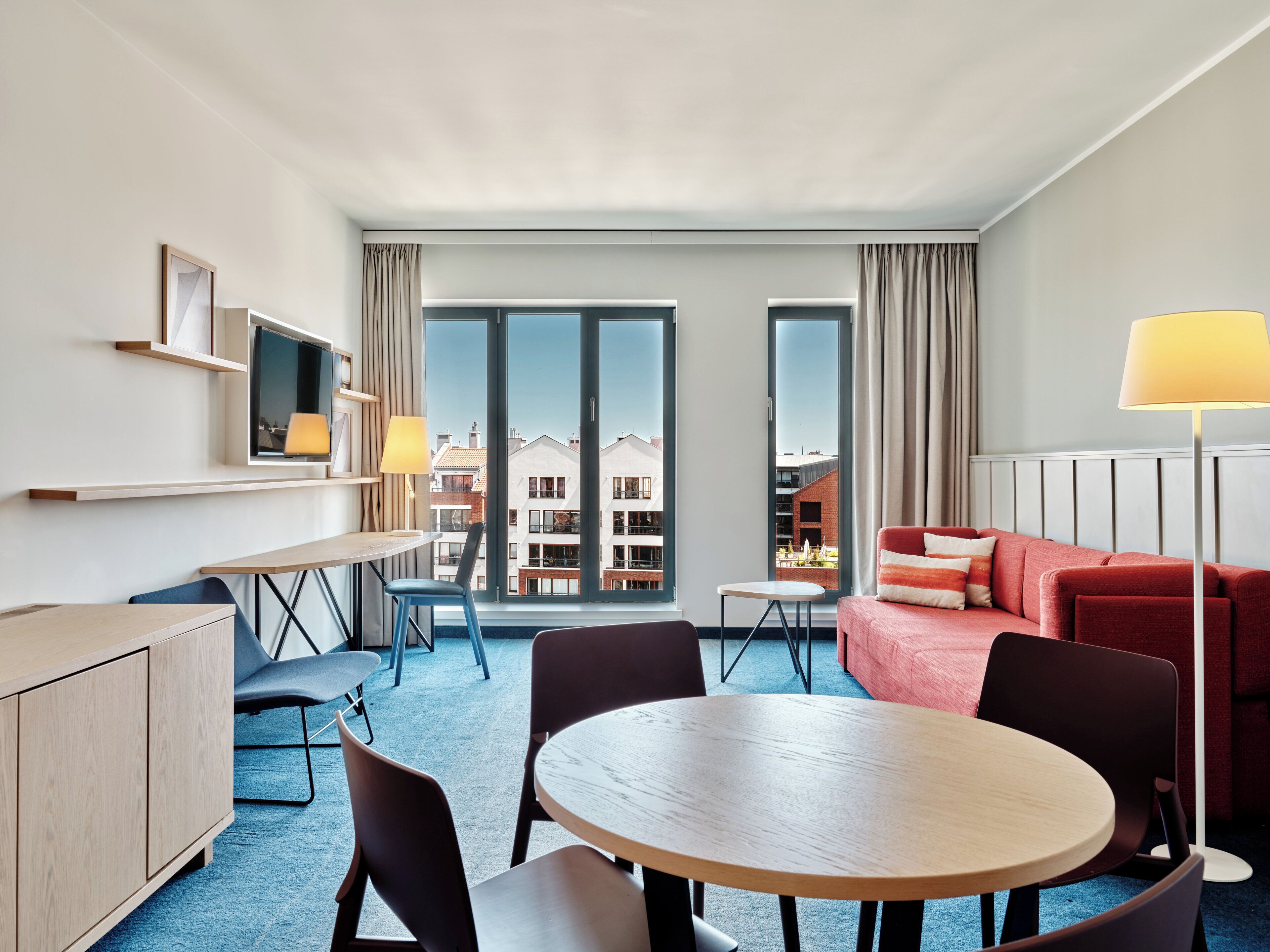 Une chambre d’hôtel moderne avec un coin repas, un canapé, une télévision et une vue sur les bâtiments.