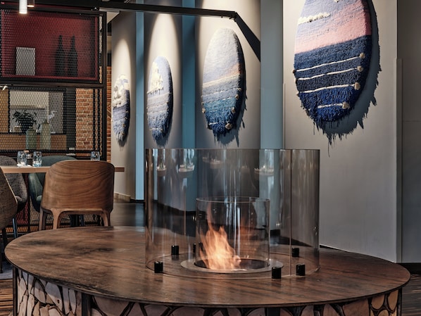 Um interior moderno com uma mesa redonda de madeira, lareira em vidro e arte abstrata nas paredes.