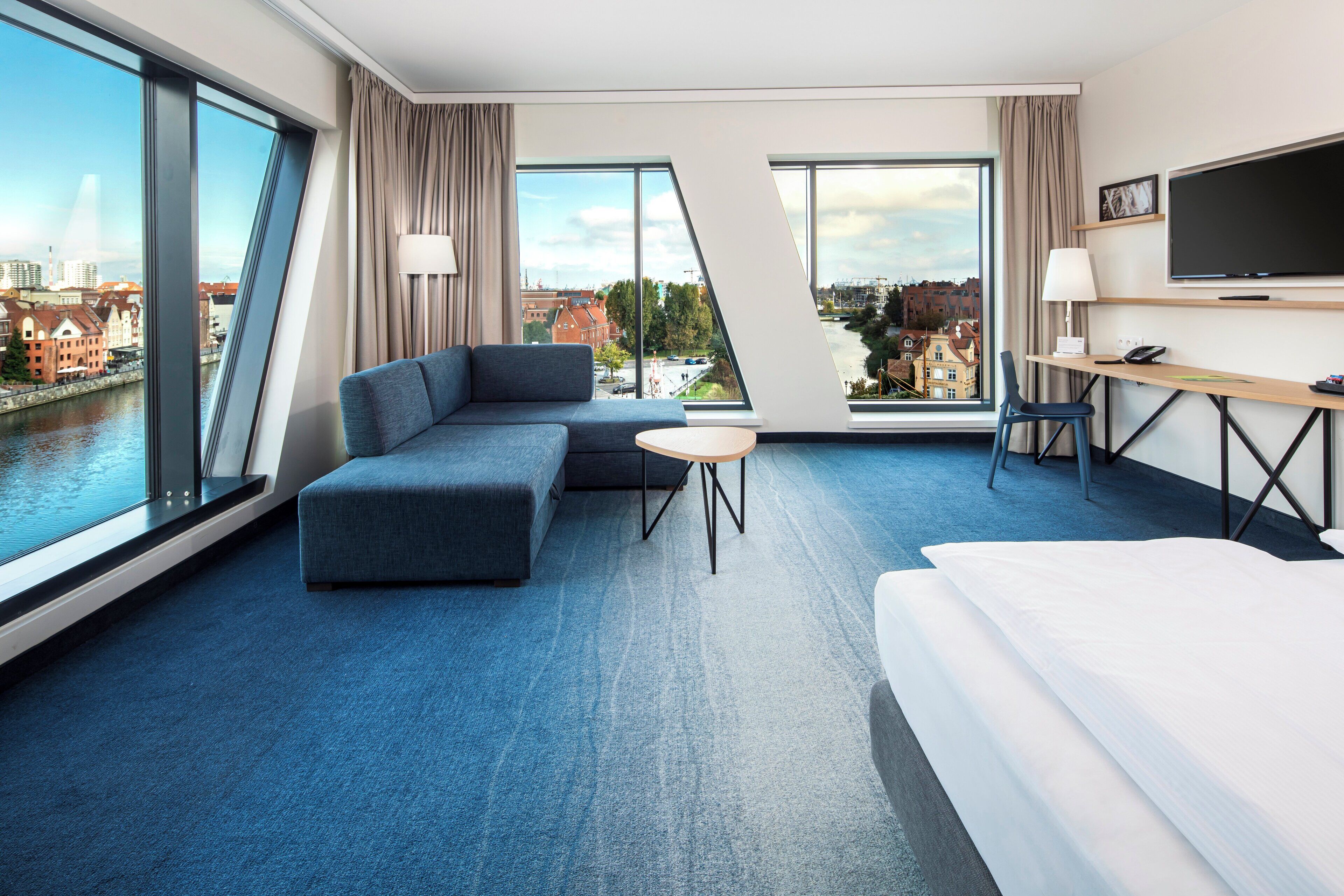 Une chambre d’hôtel moderne avec un grand lit, un canapé, une petite table et un bureau avec une télévision.