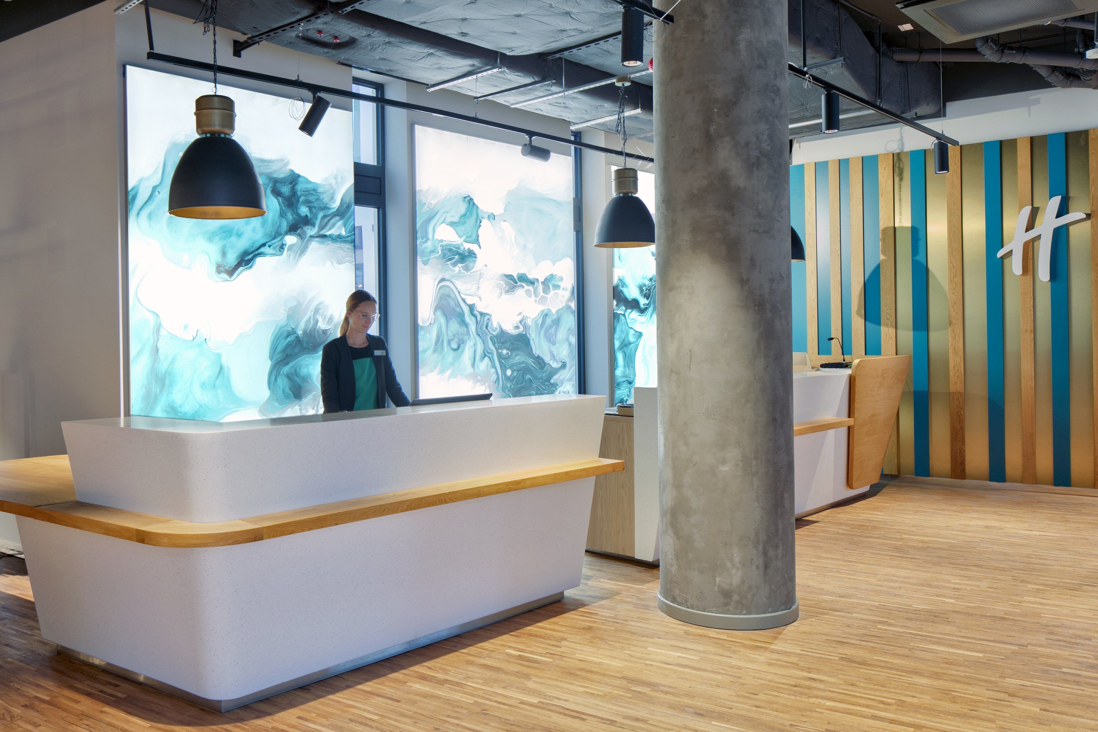 Un espace d’accueil au design moderne, comprenant une grande fenêtre offrant une vue sur un paysage montagneux, un comptoir d’accueil et un mur décoratif en bois orné d’un logo.