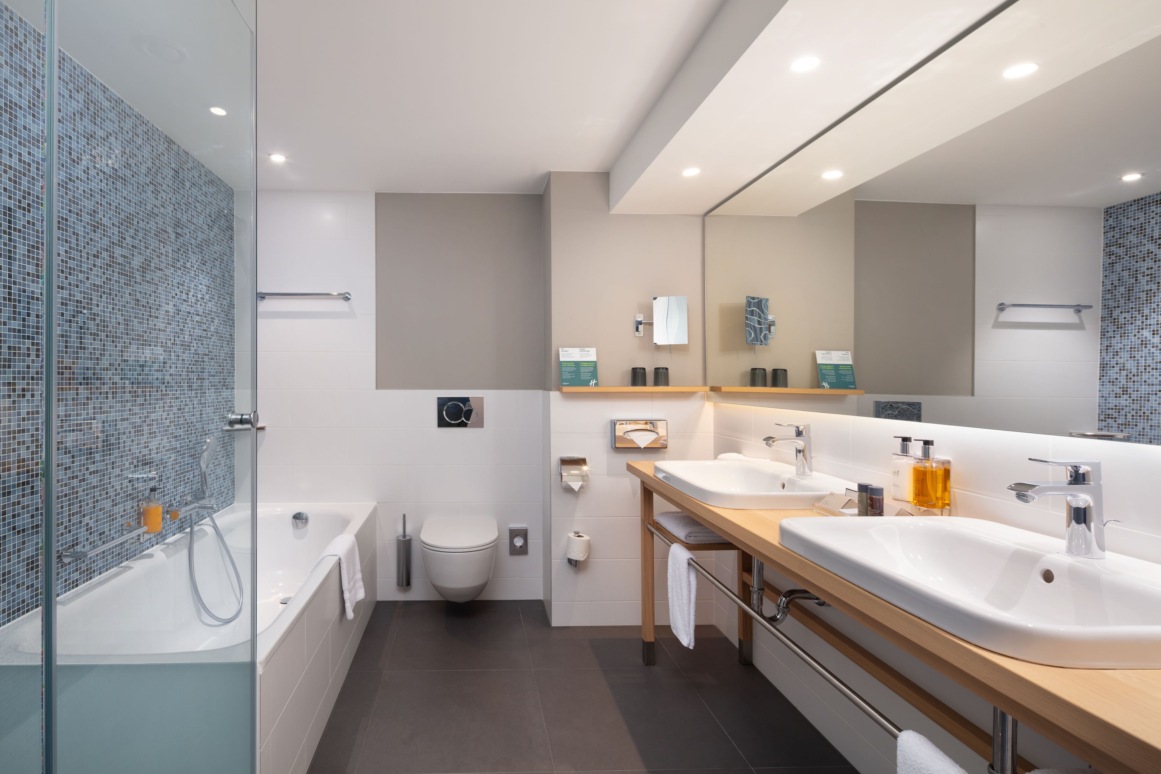 A modern bathroom with a glass-enclosed shower, a white toilet, and a vanity with two sinks and a mirror.