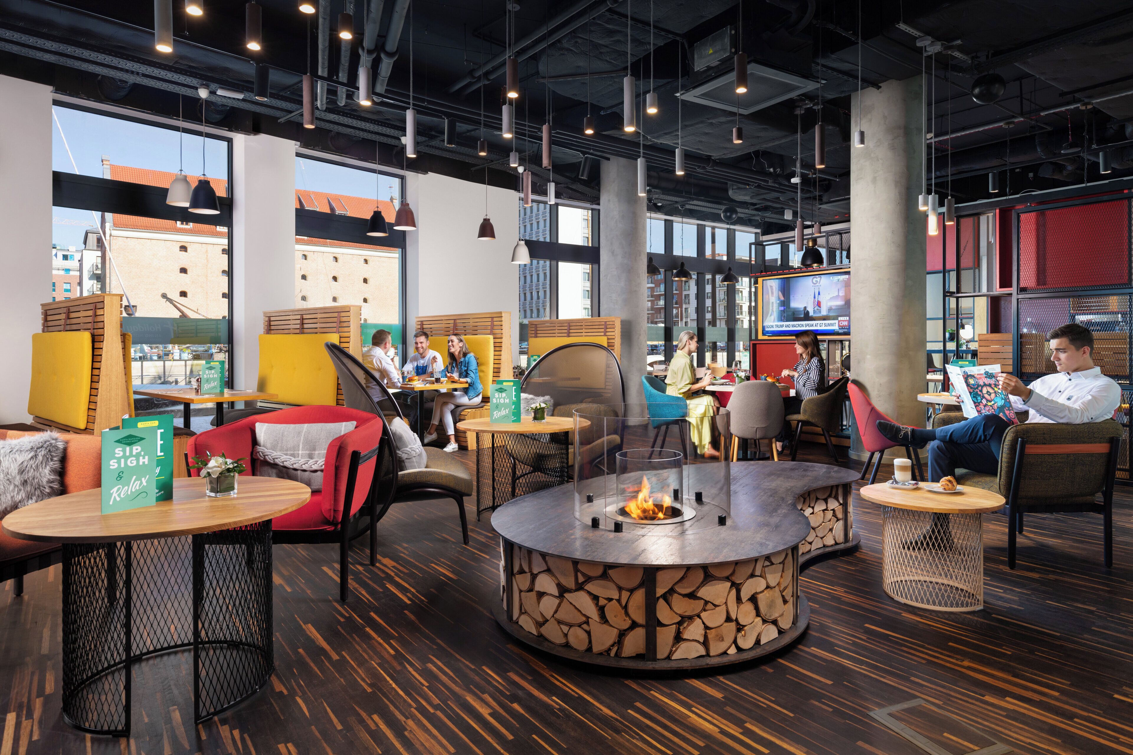 A modern lounge area with round tables, comfortable seating, and a central fire feature.
