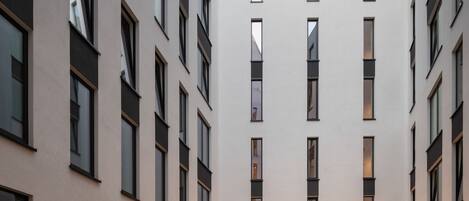 Un edificio moderno con un patio interior, varios pisos, ventanas amplias y zonas de estar al aire libre con guirnaldas de luces.