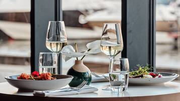 Une table à manger avec un saladier de pâtes, un vase de fleurs et deux verres à vin.