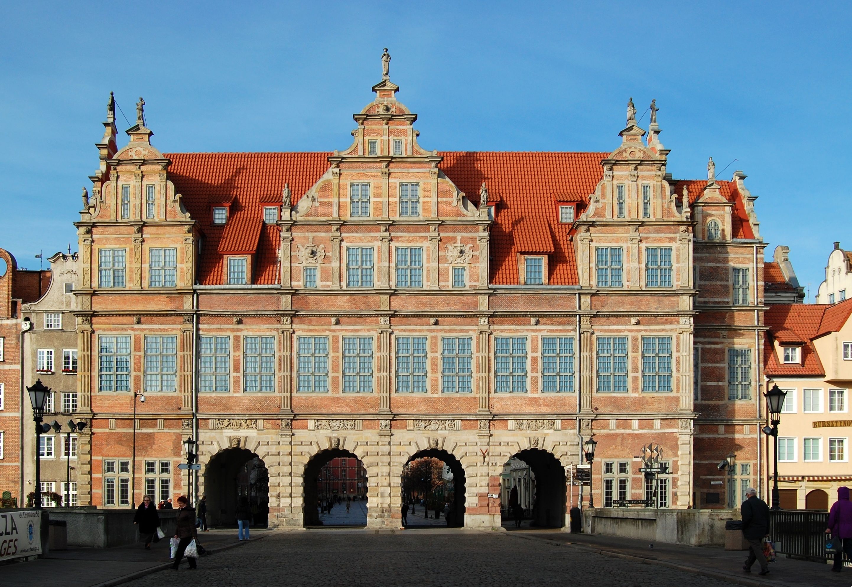 Ein historisches Gebäude mit einer symmetrischen Fassade, großen Bogenportalen und einem zentralen Uhrturm.