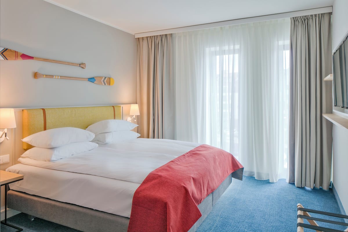 A hotel room with a bed, a nightstand, a lamp, a TV, and a window with curtains.