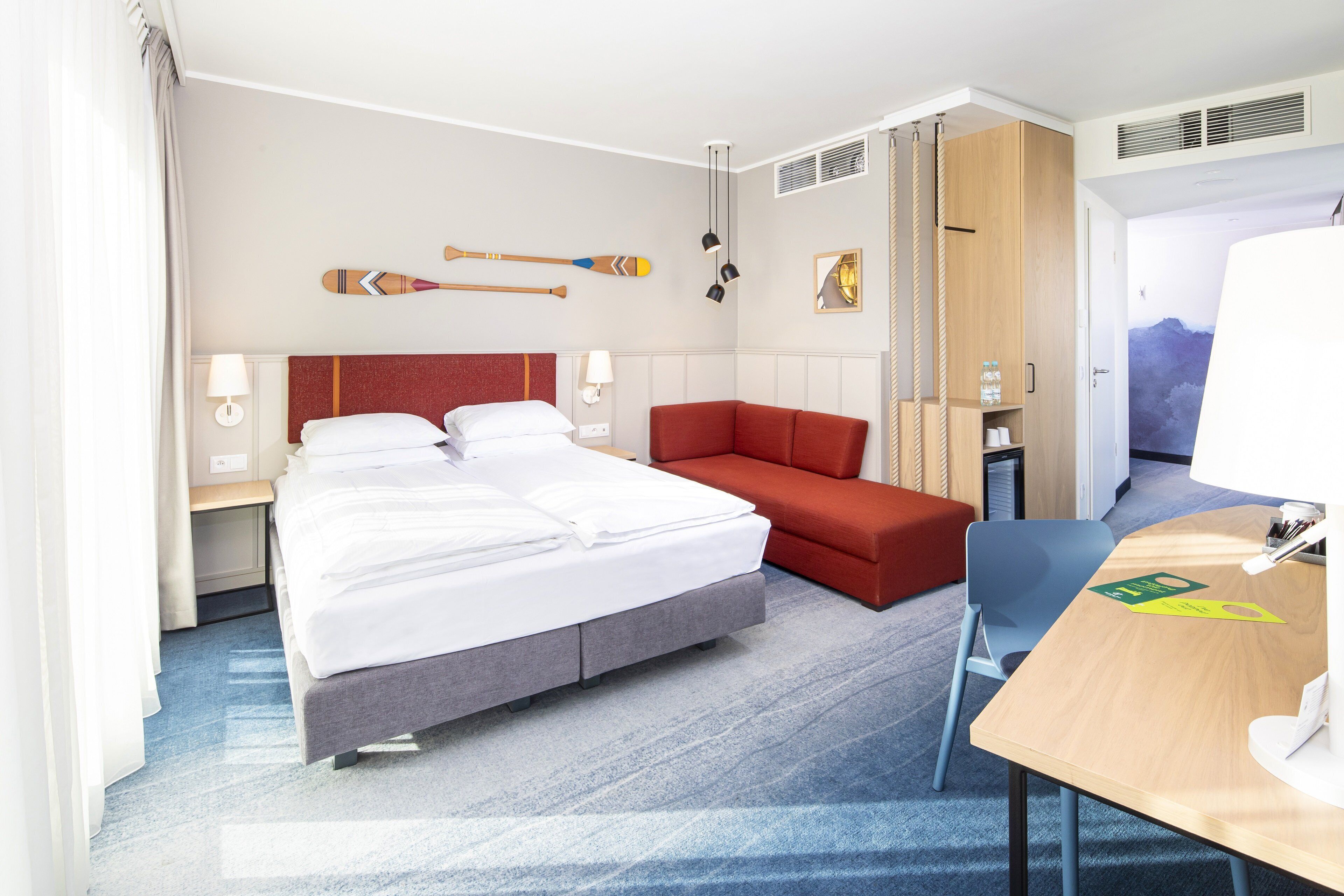Une chambre d’hôtel avec un lit, un bureau, un canapé rouge et un téléviseur fixé au mur.