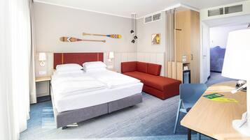 Une chambre d’hôtel avec un lit, un bureau, un canapé rouge et un téléviseur fixé au mur.