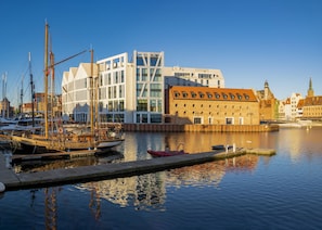 A marina with boats docked, a modern building with large windows, and a historic brick building with a clock tower in the background. - Holiday Inn Gdansk - City Centre by IHG (Gdansk)