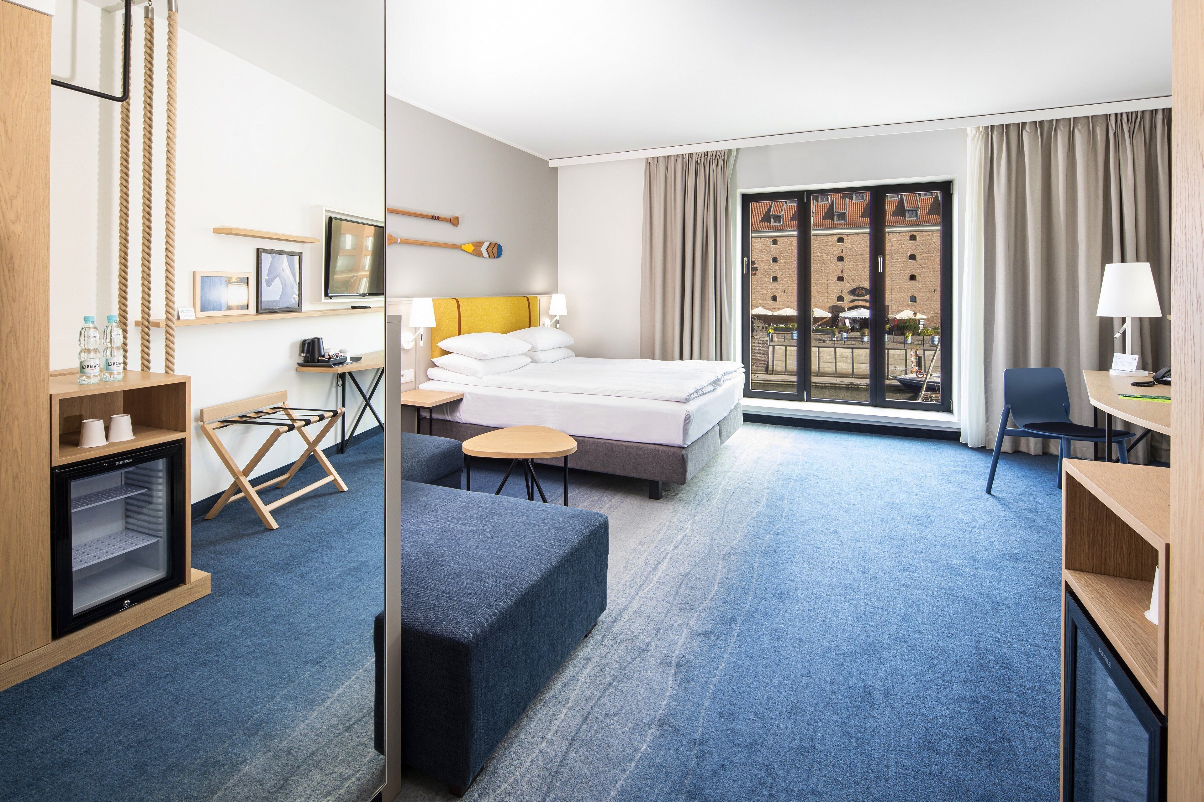 Ein Hotelzimmer mit Bett, Schreibtisch, Stuhl, kleinem Tisch, Fernseher und einem Fenster mit Vorhängen.