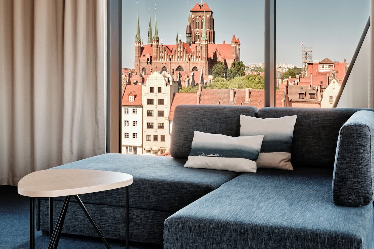 A modern living room with a grey sofa, a small white table, and a view of a historic church through large windows.