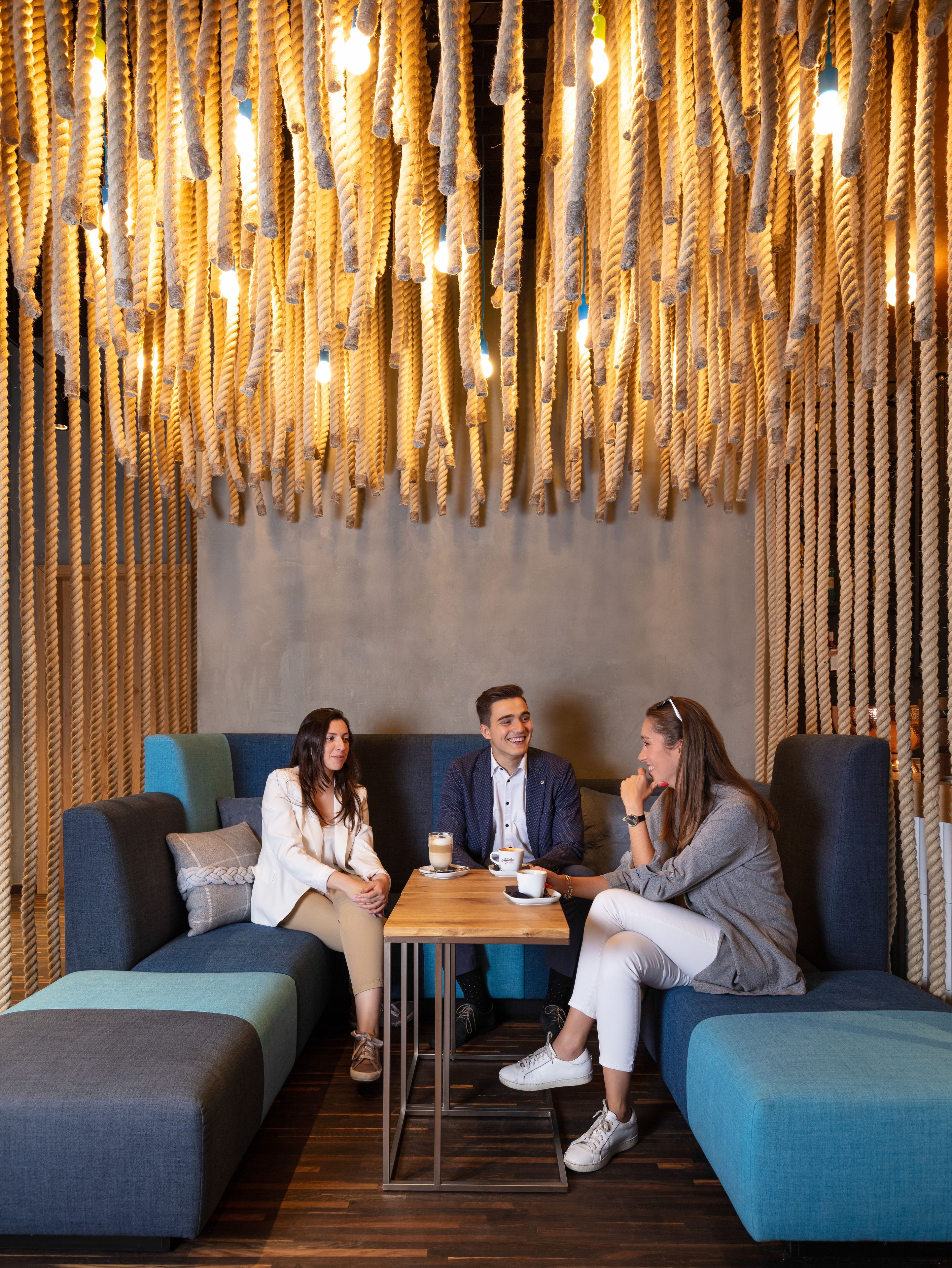 A modern lounge area with a wooden floor, blue sofas, and a hanging light fixture.