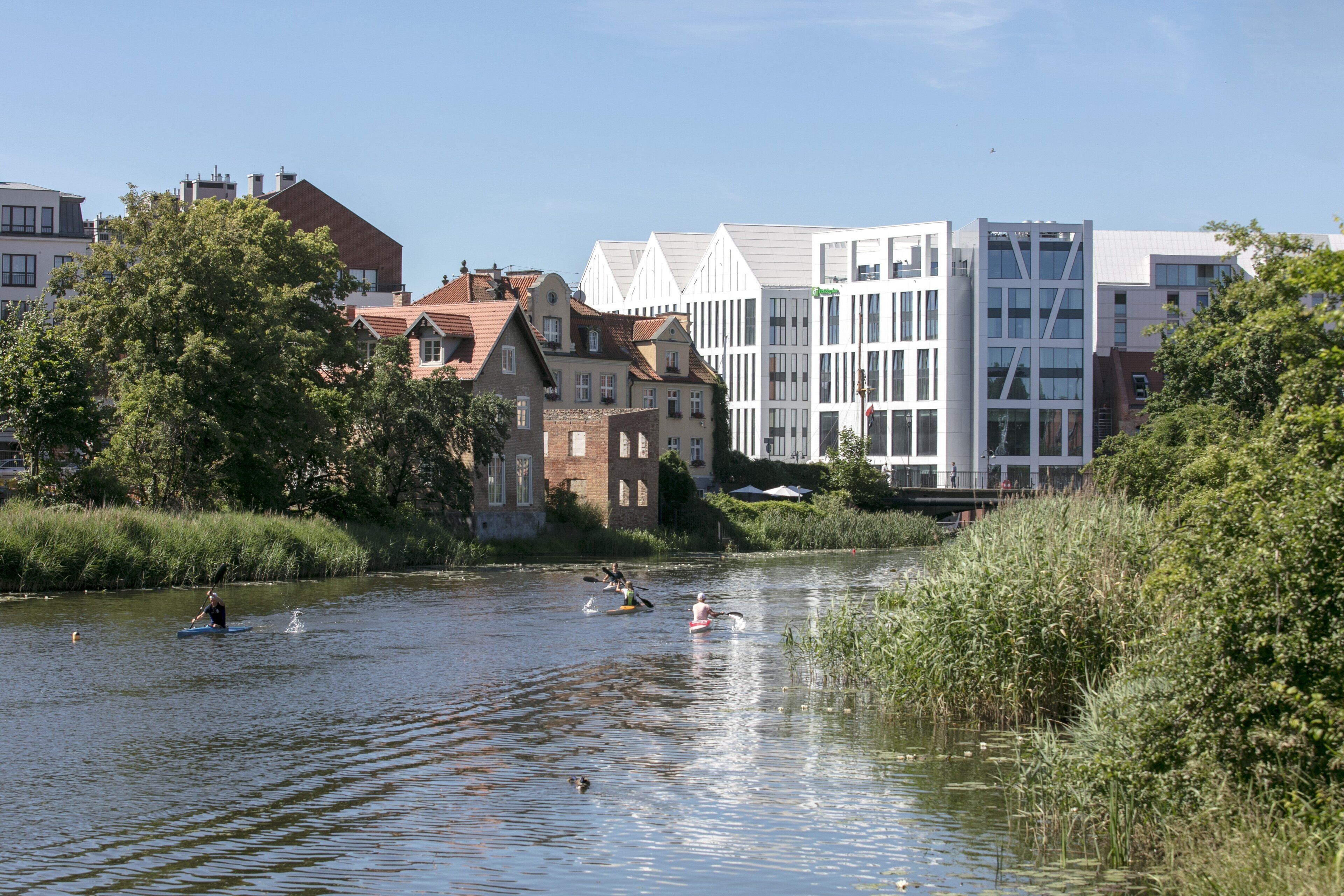 A river with people kayaking, surrounded by buildings with varied architecture.
