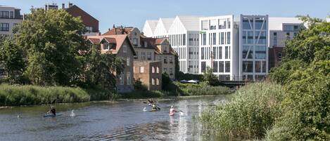 Un río con personas haciendo kayak, rodeado de edificios de arquitectura variada.