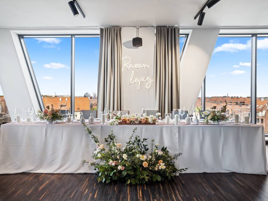 Una mesa para recepción de bodas con manteles blancos, centros de mesa florales y velas.