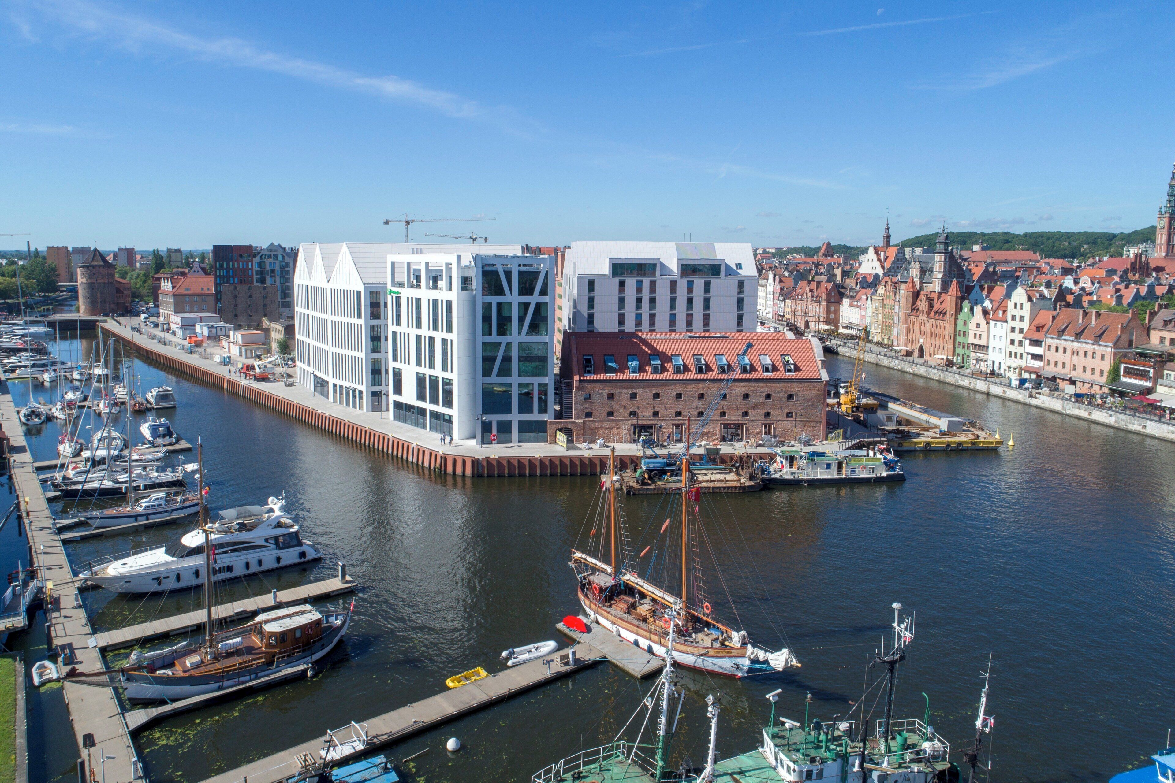 A marina with boats docked, a modern building, and traditional architecture in the background.