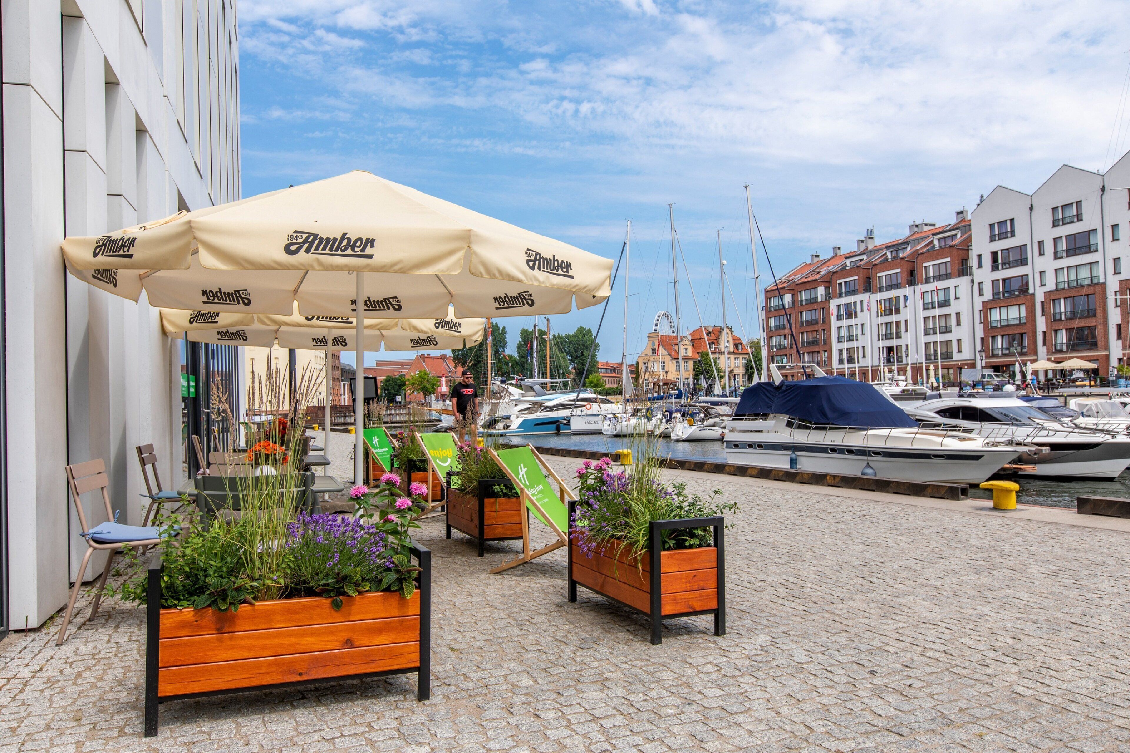 A waterfront café with outdoor seating, a large umbrella, and a view of boats and buildings.