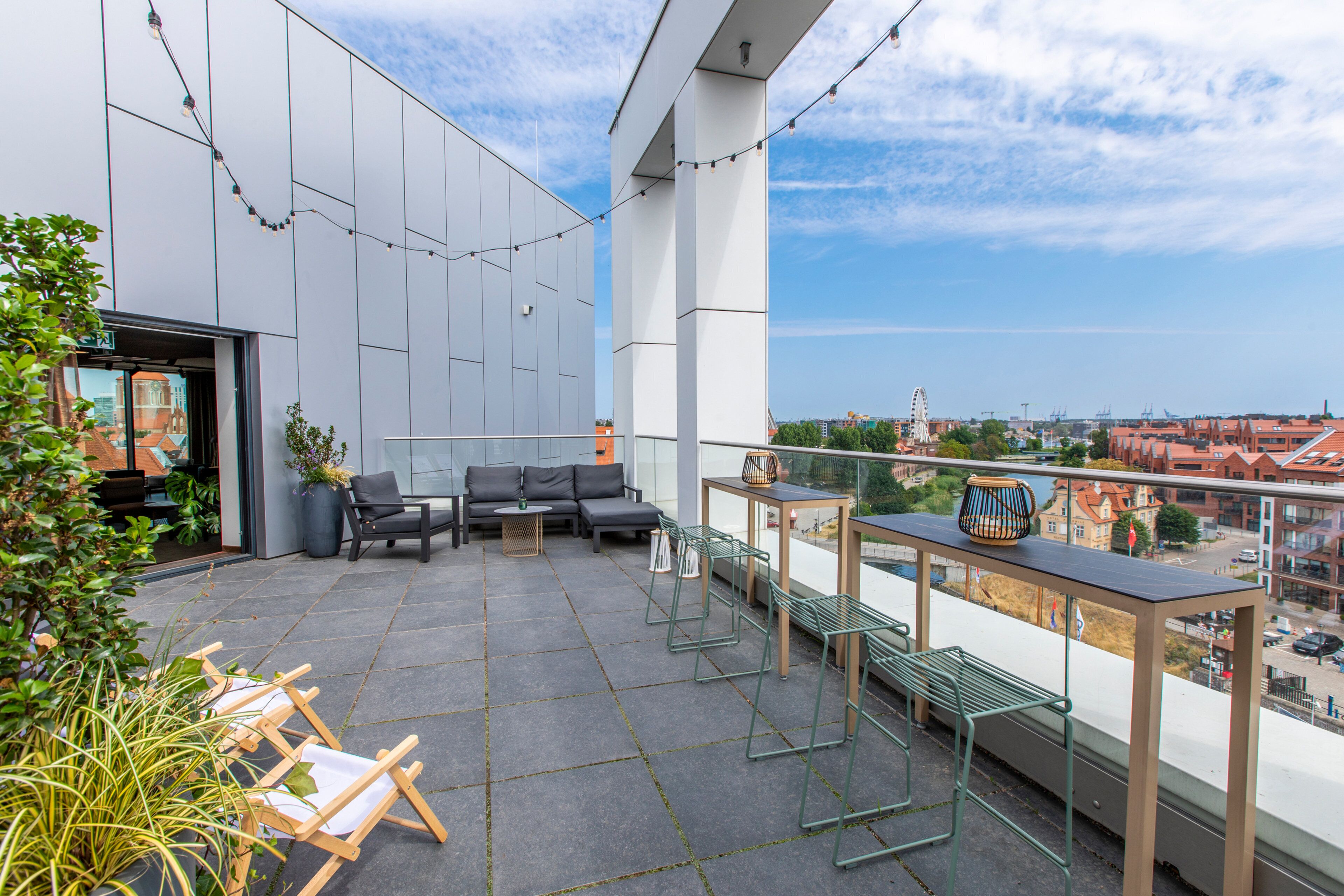 A modern outdoor terrace with a sofa, chairs, and a table, overlooking a cityscape.