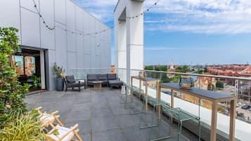 En moderne udendørs terrasse med sofa, stole og et bord, med udsigt over bybilledet.