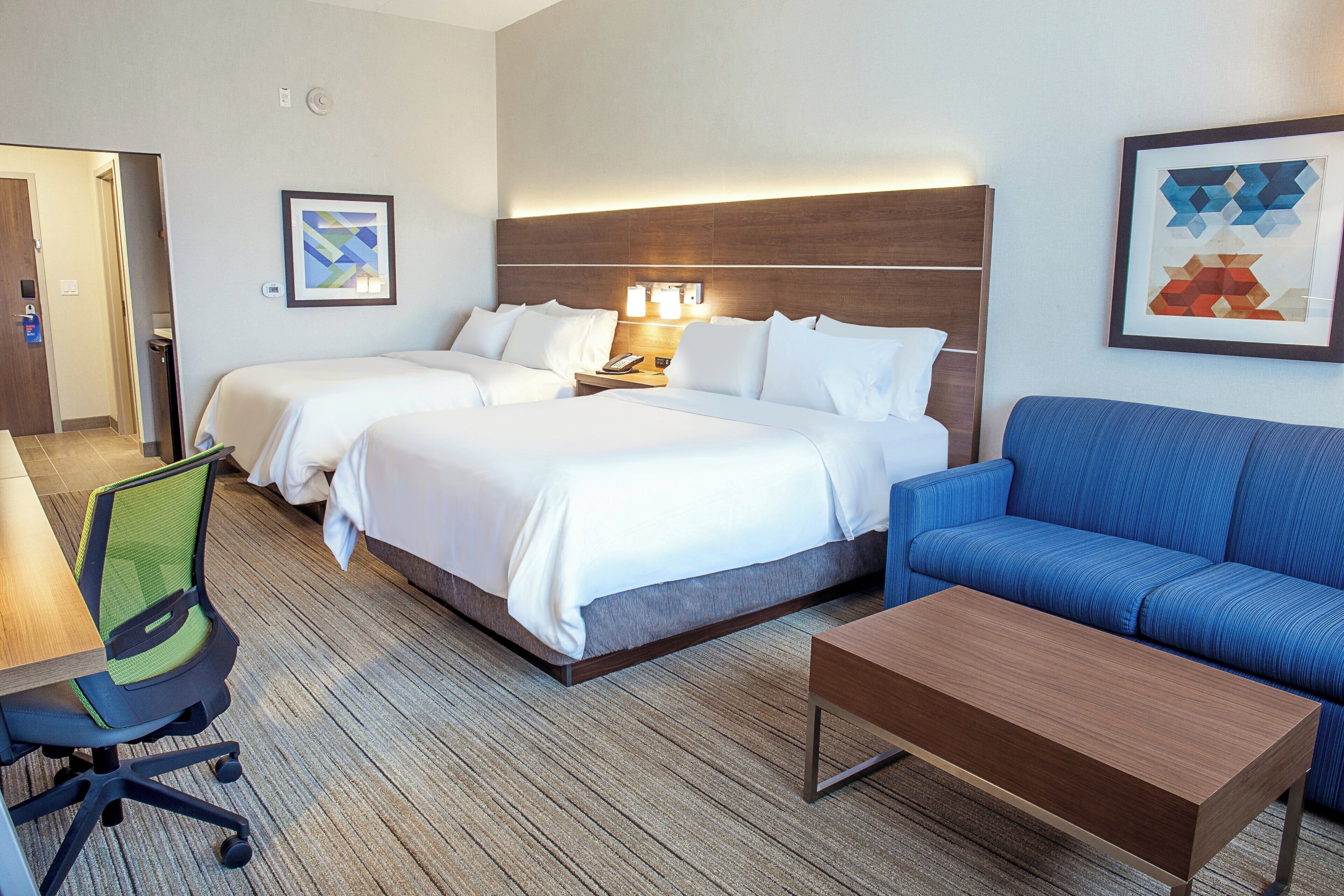 A hotel room with two beds, a sofa, a desk, and a chair.