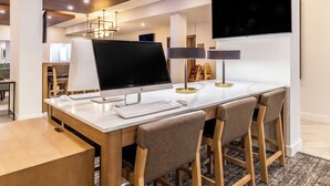 A modern hotel room with a large desk, a flat-screen TV, and a comfortable seating area with bar stools.