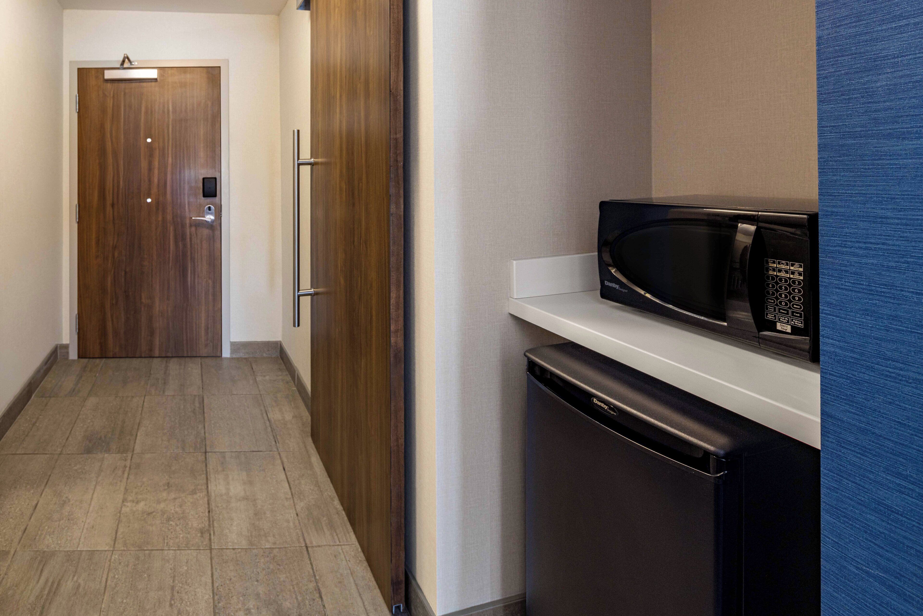 A narrow hallway with a wooden door, a microwave on a white countertop, and a dishwasher.