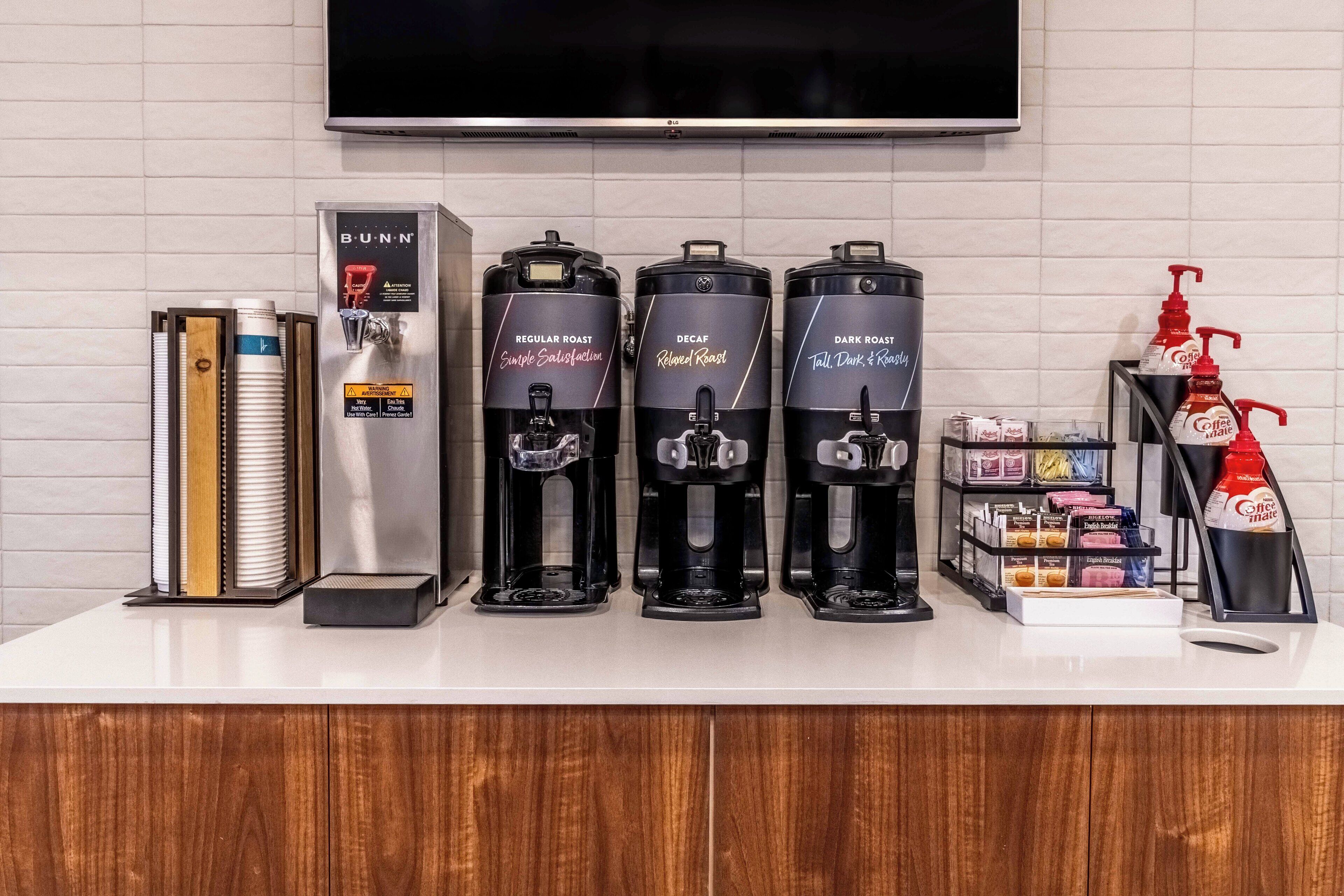 A coffee station with three coffee makers labeled Regular Roast, Decaf, and Dark Roast. There are also coffee pods and a coffee maker on the left.