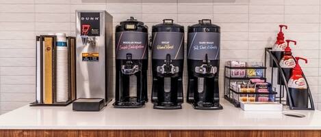 A coffee station with three coffee makers labeled Regular Roast, Decaf, and Dark Roast. There are also coffee pods and a coffee maker on the left.