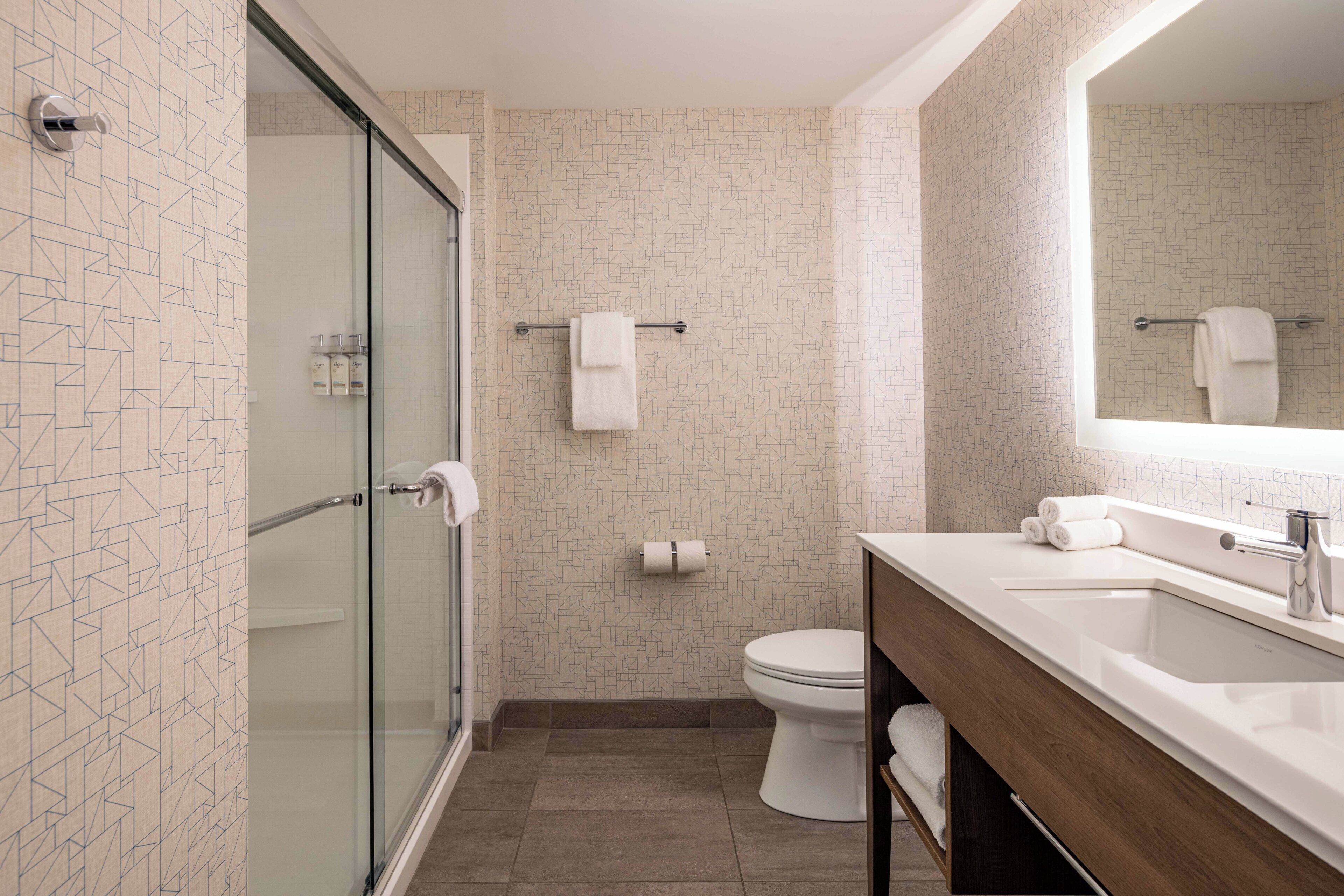 Un baño moderno con cabina de ducha de vidrio, un inodoro y un lavamanos con espejo.