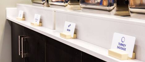 A buffet setup with labeled containers for bacon, turkey sausage, and scrambled eggs.
