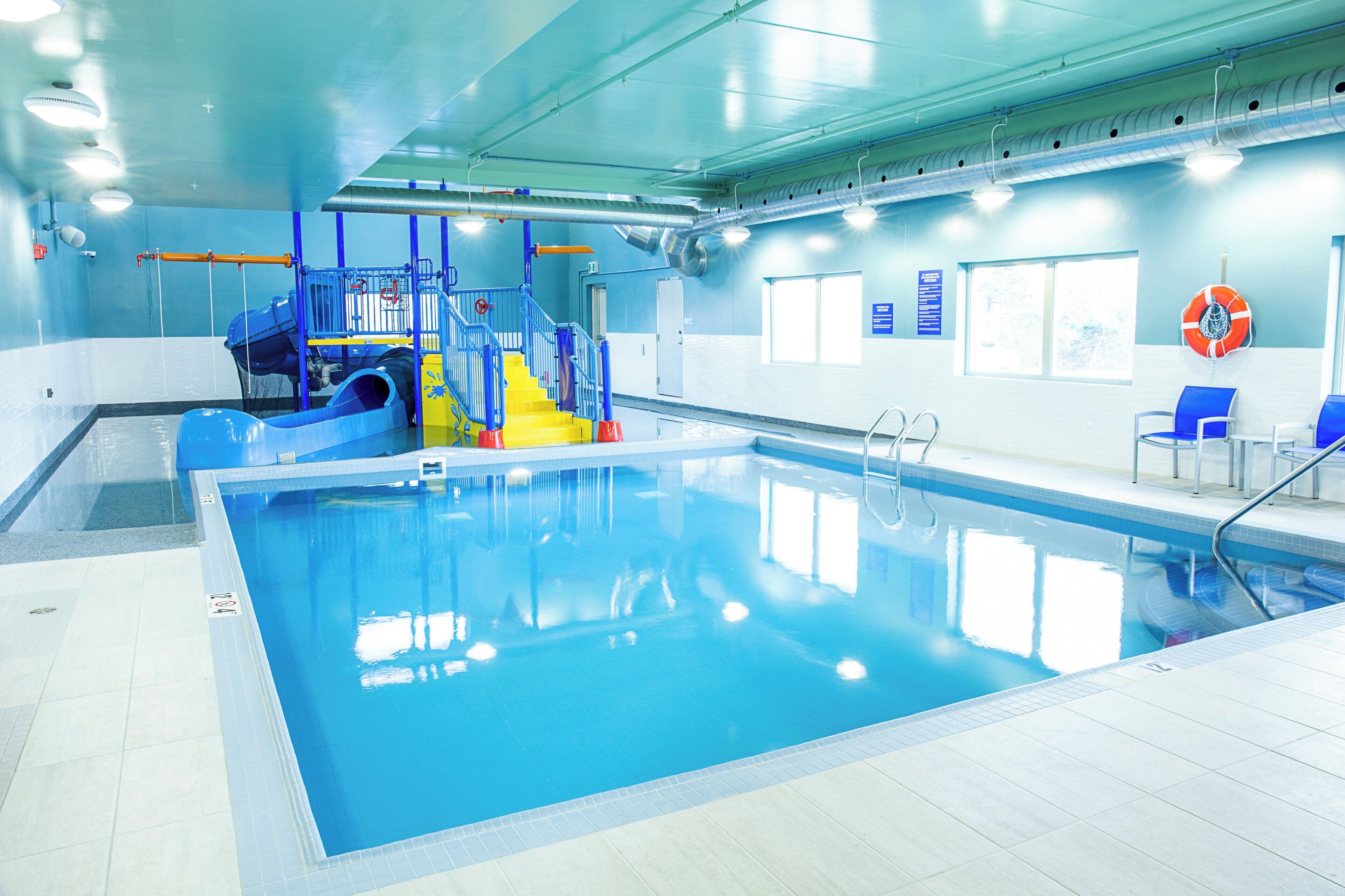 Una piscina interior con tobogán, sillas azules y un flotador en la pared.
