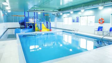 Una piscina interior con tobogán, sillas azules y un flotador en la pared.