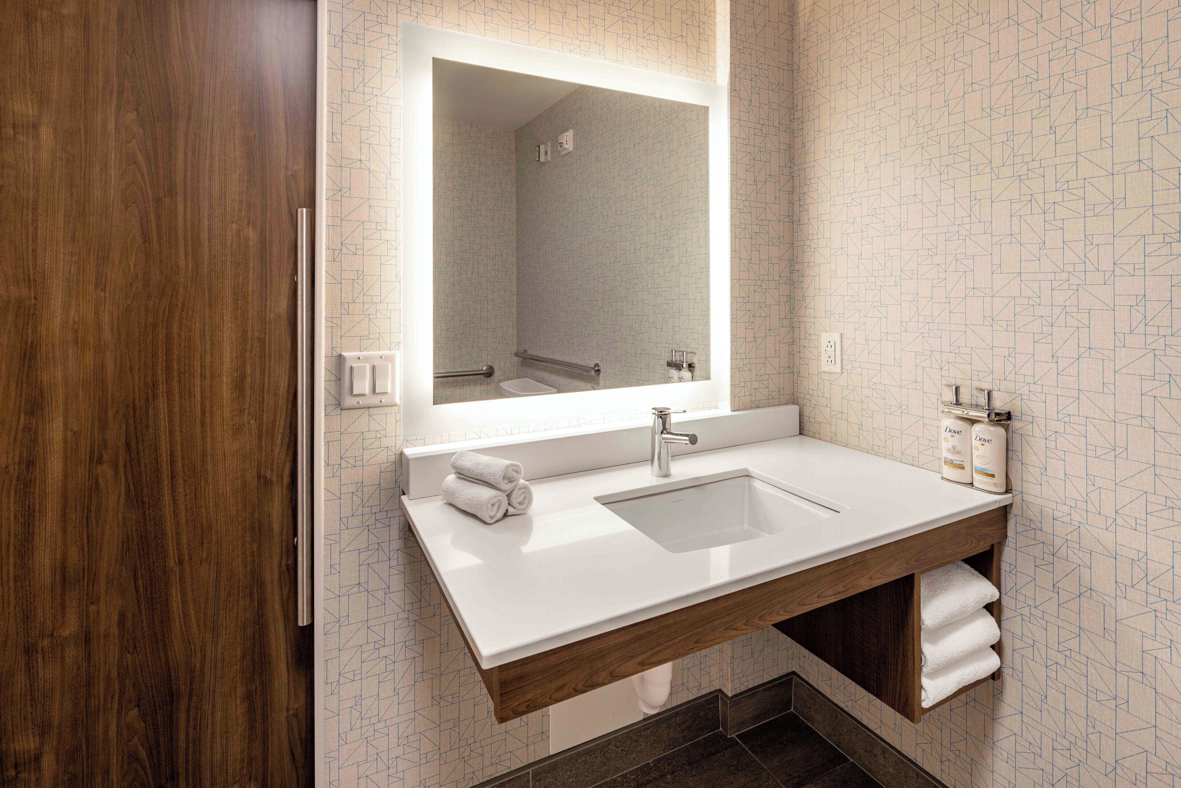 A modern bathroom with a wooden vanity, a large mirror, and a built-in sink.