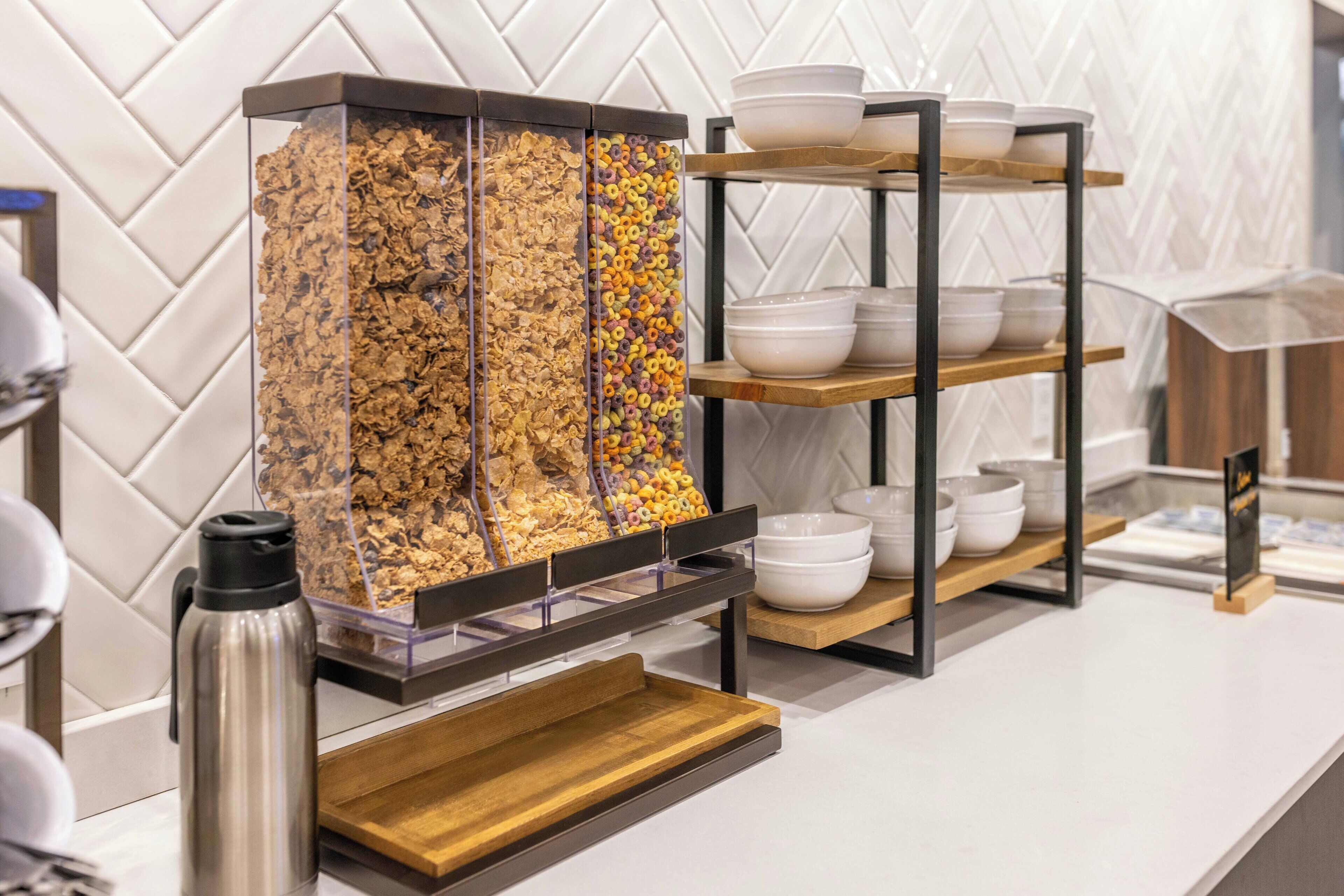 A breakfast buffet with cereal and bowls on shelves.