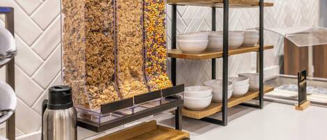 A breakfast buffet with cereal and bowls on shelves.