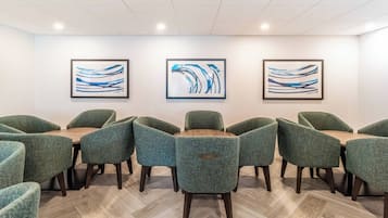 Un salón de conferencias con una mesa redonda y sillas tapizadas de verde, arte abstracto enmarcados en las paredes y un suelo de madera con motivo de espiga.
