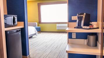 Habitación de hotel compacta con kitchenette, cama, ventana y un pequeño rincón de descanso.